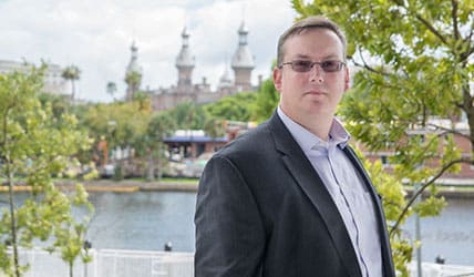 A man in a suit standing next to a lake.